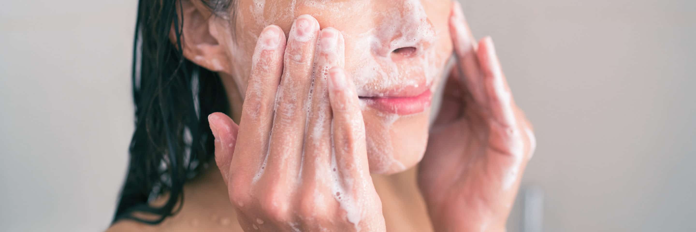 An image of a woman thoroughly cleansing her face with a white lather.